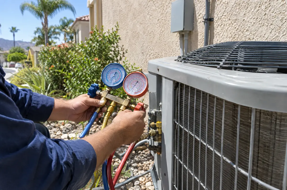 An HVAC technician checking gauges on an outdoor air conditioning unit